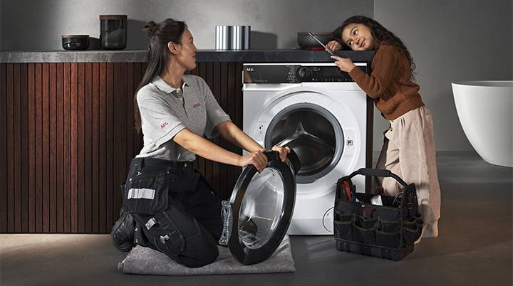 Woman unpacking spare parts for dishwashing, while smiling at a black dog with a toy in its mouth